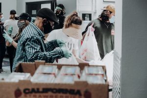 Volunteers wearing gloves and mask place food in plastic bags for donations
