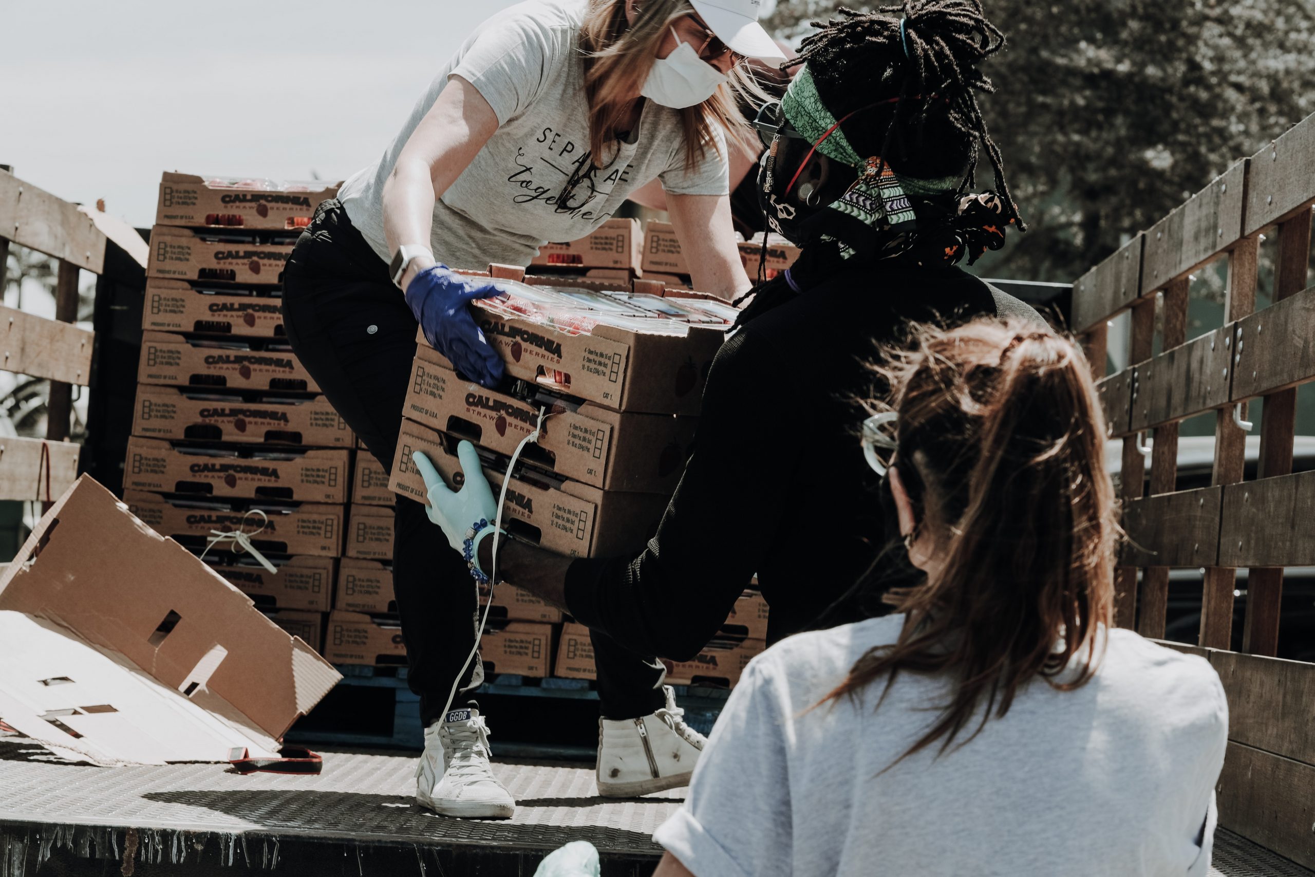 Three volunteers wearing face masks unload crates of strawberries off of a truck
